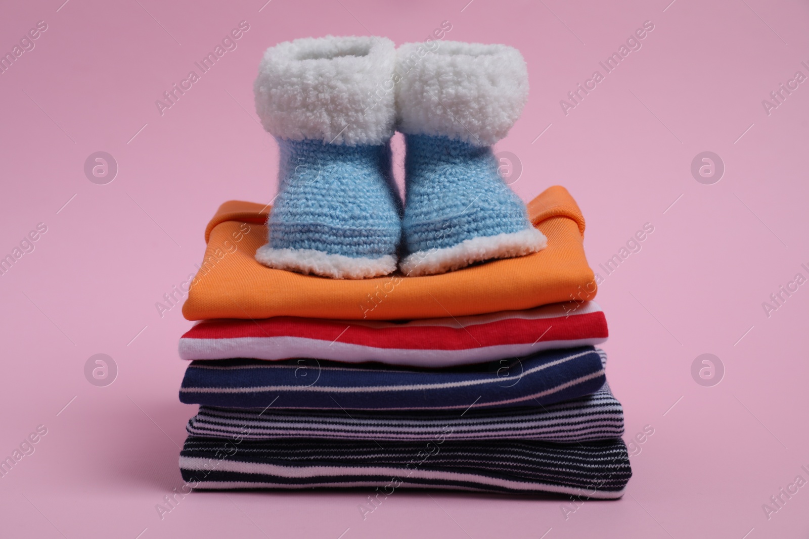 Photo of Stack of clean baby clothes and small booties on pink background