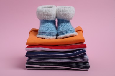 Stack of clean baby clothes and small booties on pink background