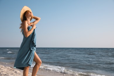 Attractive woman with beach towel and straw hat near sea, space for text