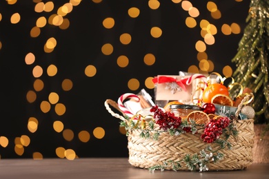 Photo of Wicker basket with Christmas gift set on wooden table against blurred festive lights. Space for text