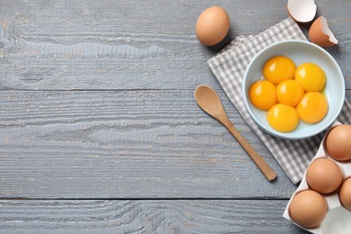 Photo of Chicken eggs and bowl with raw yolks on grey wooden table, flat lay. Space for text