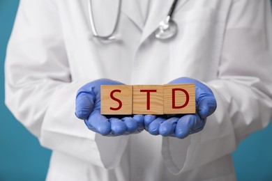 Photo of Doctor holding wooden cubes with abbreviation STD on light blue background, closeup
