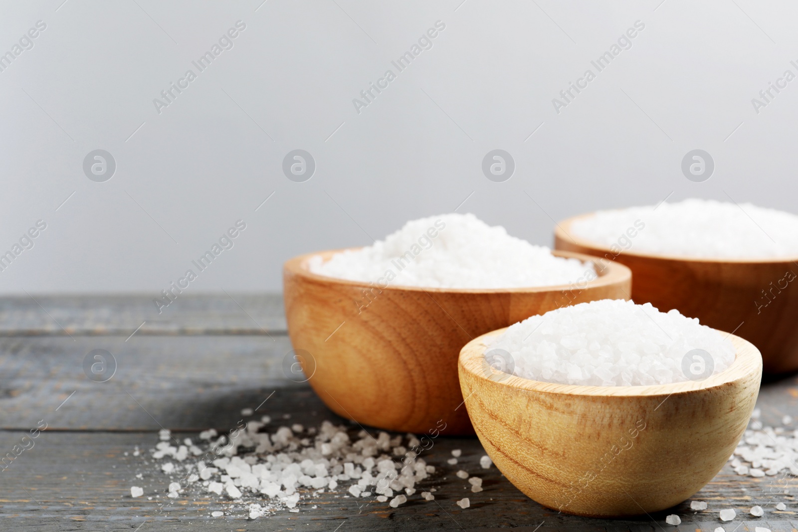 Photo of Bowls of natural sea salt on grey wooden table, space for text