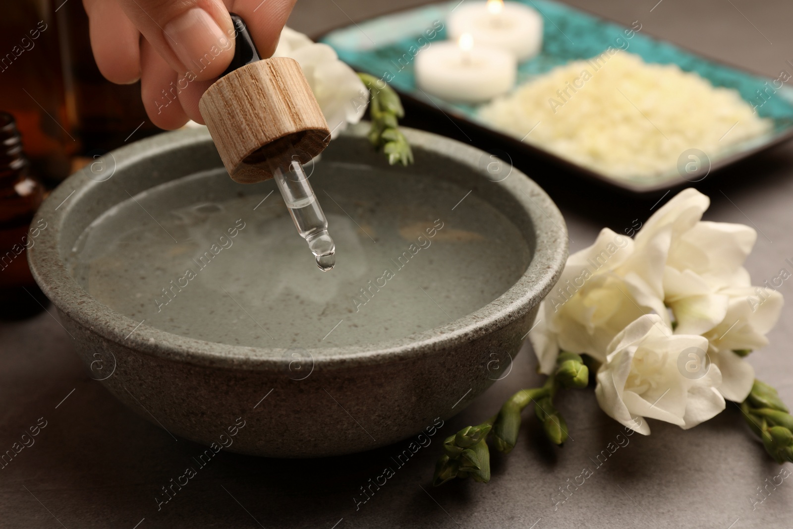 Photo of Woman dripping essential oil into bowl at grey table, closeup. Aromatherapy treatment