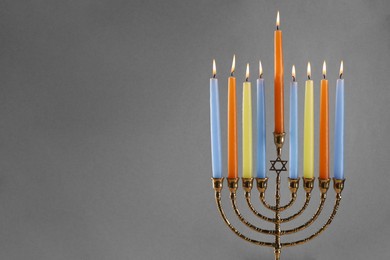 Photo of Hanukkah celebration. Menorah with burning candles on grey background, closeup. Space for text