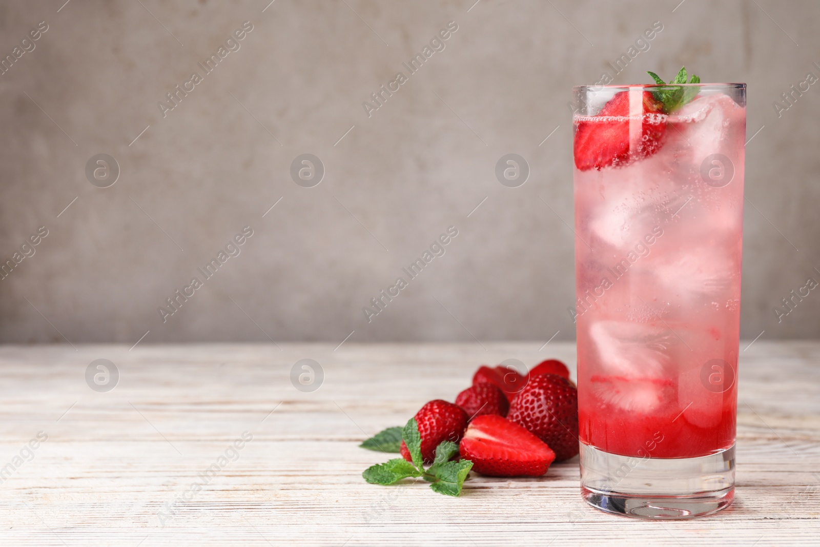 Photo of Glass of refreshing drink with strawberry and mint on light wooden table against grey background, space for text