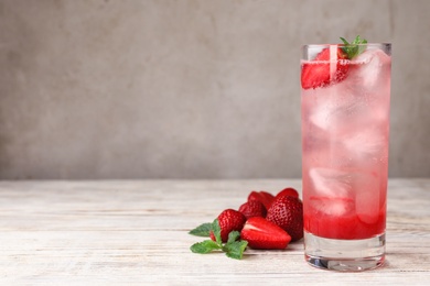 Glass of refreshing drink with strawberry and mint on light wooden table against grey background, space for text