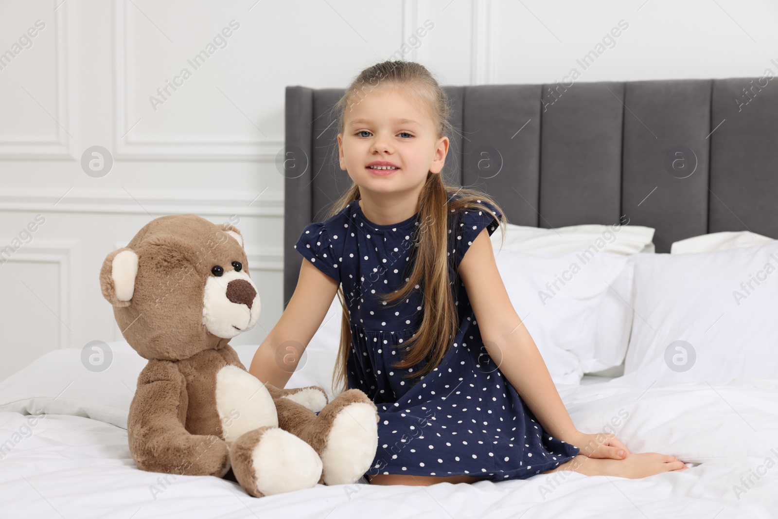 Photo of Cute little girl with teddy bear on bed