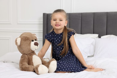 Cute little girl with teddy bear on bed