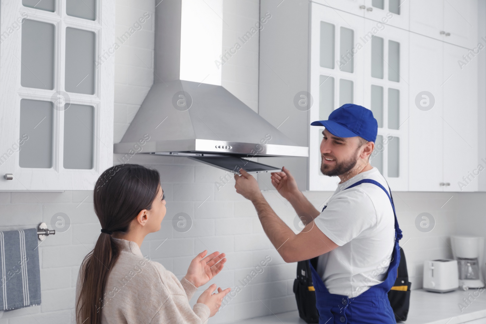 Photo of Worker repairing modern cooker hood and woman in kitchen