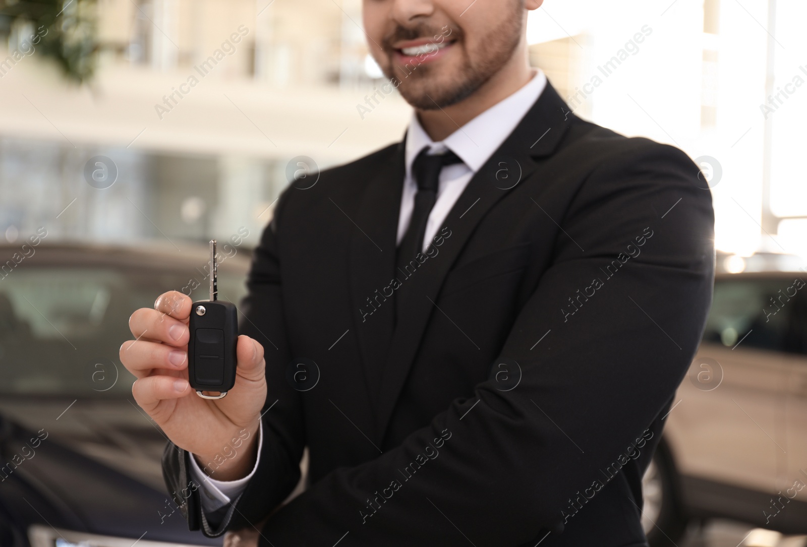 Photo of Salesman with key in modern car salon, closeup