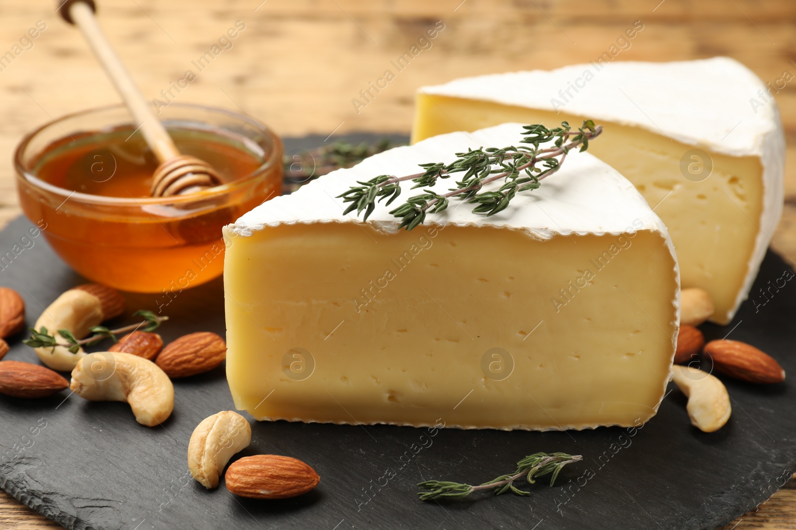 Photo of Tasty Camembert cheese with thyme, honey and nuts on slate plate, closeup