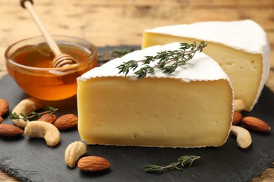 Photo of Tasty Camembert cheese with thyme, honey and nuts on slate plate, closeup