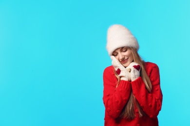 Portrait of emotional young woman in stylish hat, sweater and mittens on color background, space for text. Winter atmosphere