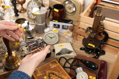 Photo of Woman holding bunch of old keys near table with different stuff, closeup. Garage sale