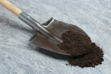 Photo of Metal shovel with fertile soil on gray textured surface