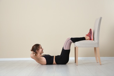 Photo of Young woman exercising with chair near color wall. Home fitness