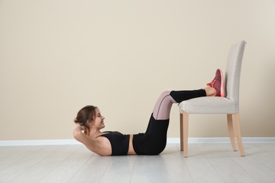 Young woman exercising with chair near color wall. Home fitness