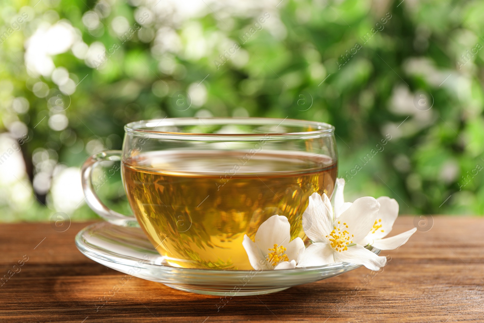 Photo of Glass cup of aromatic jasmine tea and fresh flowers on wooden table