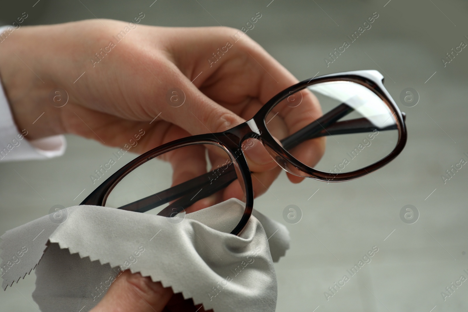 Photo of Woman cleaning glasses with microfiber cloth at home, closeup