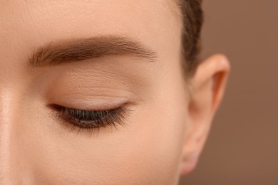 Woman with beautiful natural eyelashes on light brown background, closeup