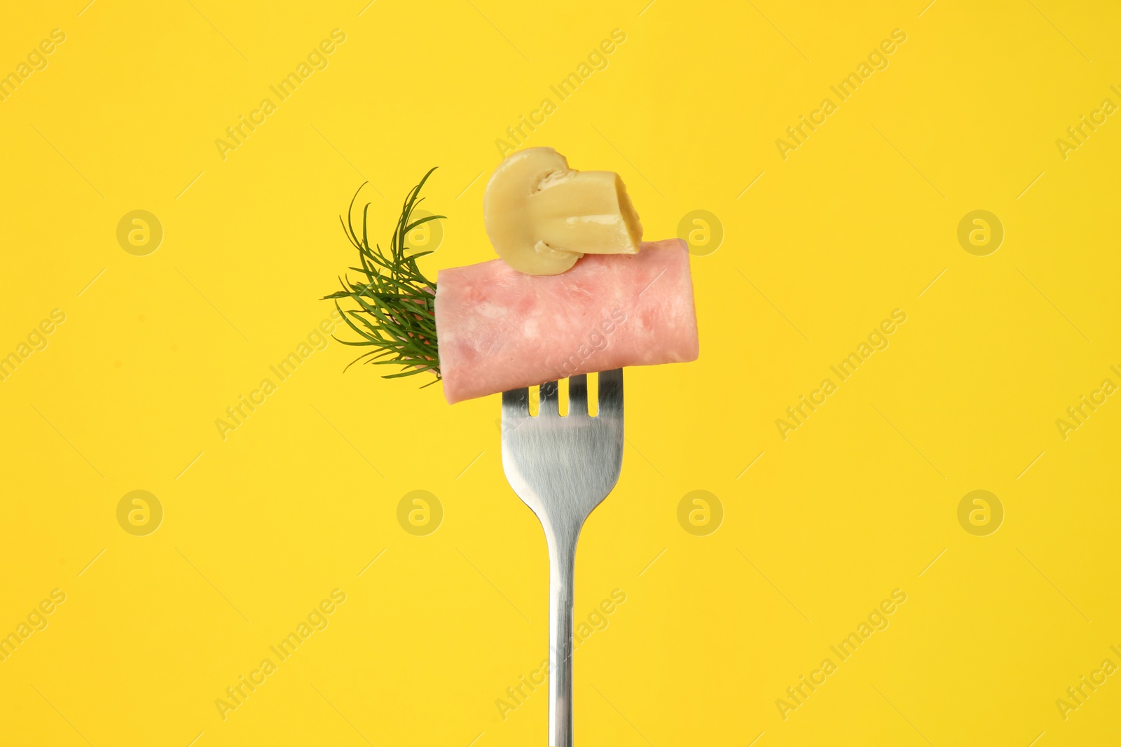 Photo of Fork with tasty slice of ham, pickled mushroom and dill on yellow background