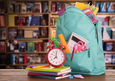 Backpack with school stationery on wooden table in library, space for text