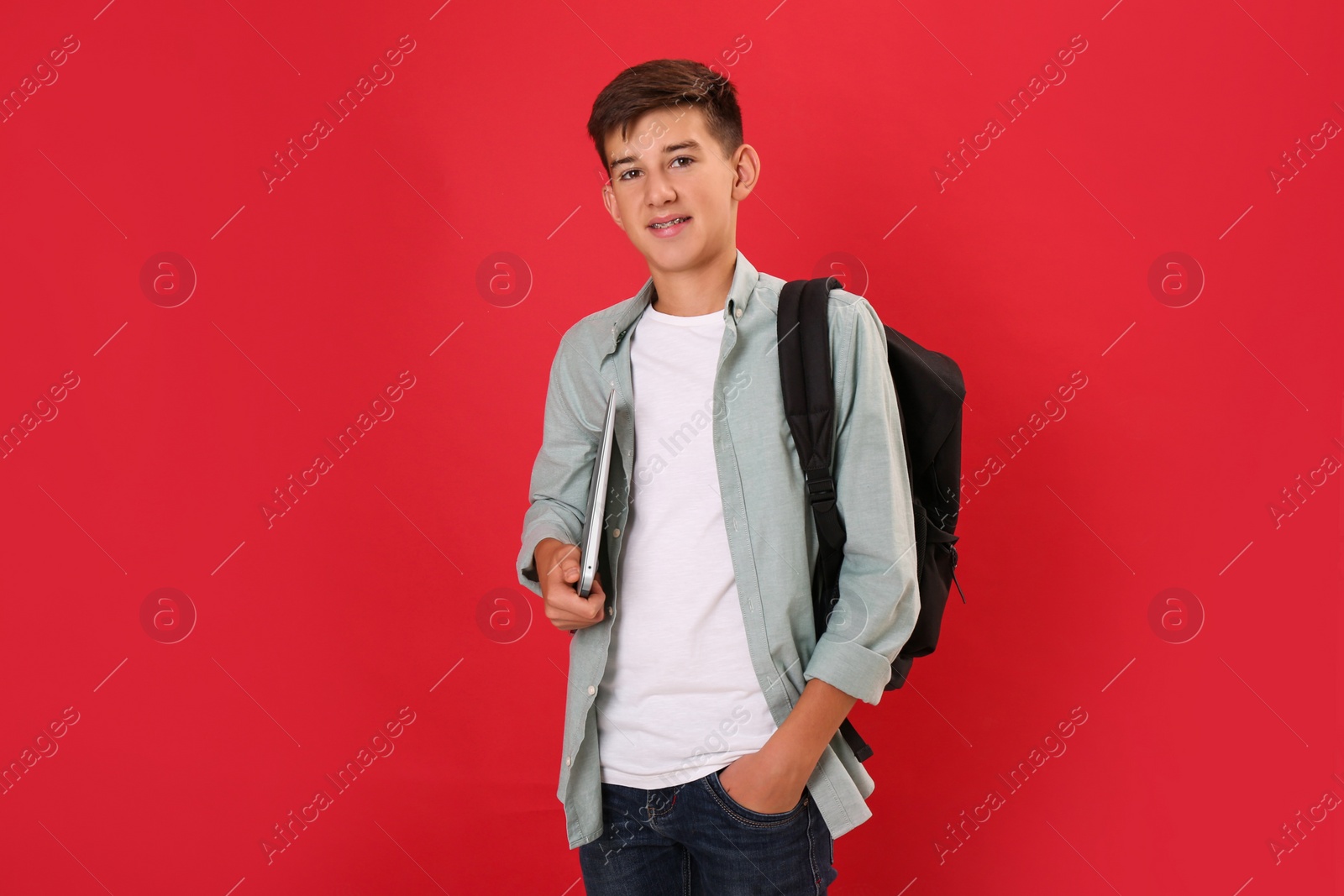 Photo of Teenage student with backpack and laptop on red background