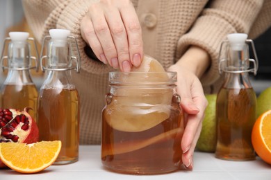 Photo of Woman making homemade fermented kombucha at white table, closeup