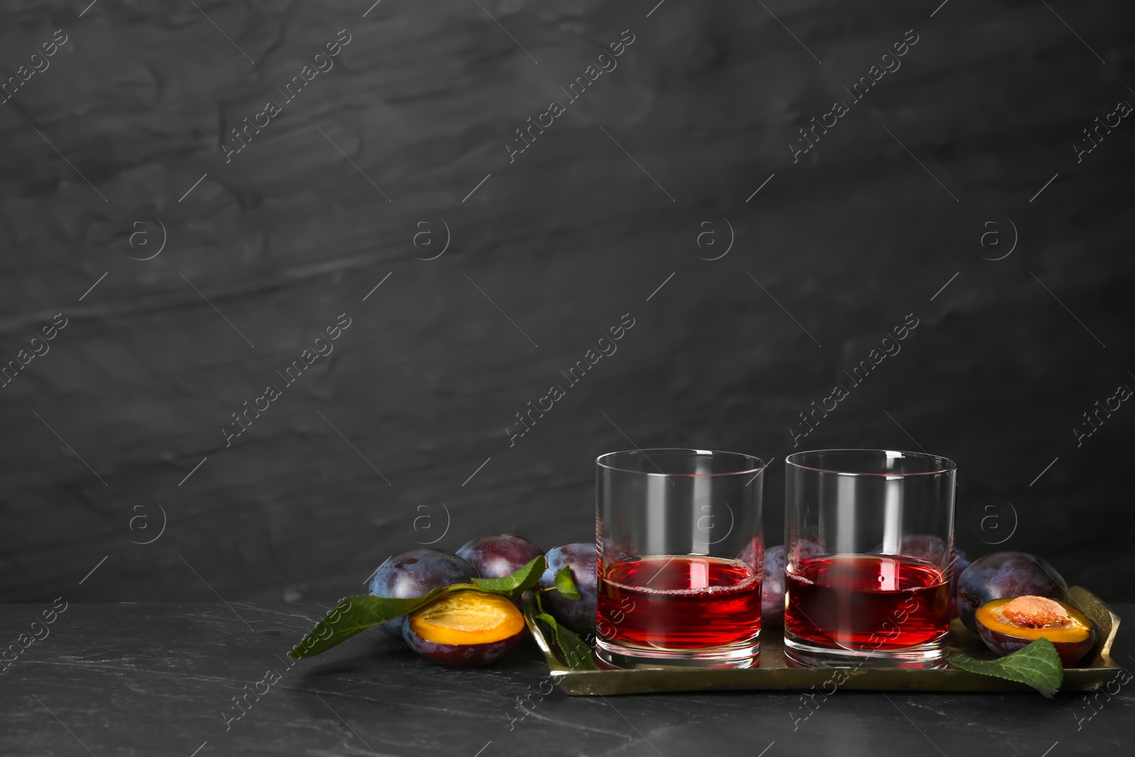 Photo of Delicious plum liquor and ripe fruits on black table. Homemade strong alcoholic beverage