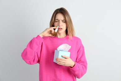 Photo of Sick young woman using nasal spray on white background