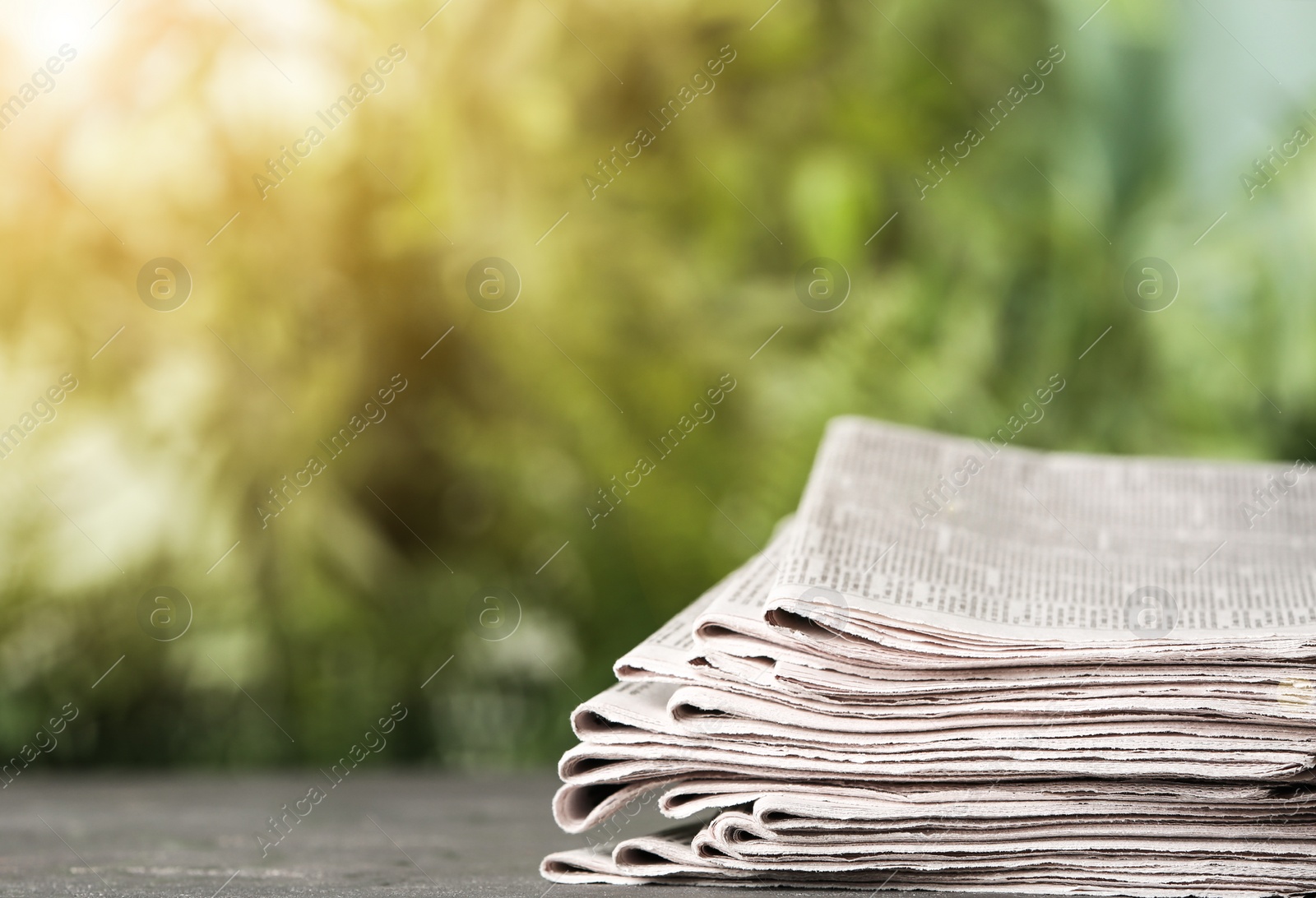 Image of Stack of newspapers on grey table against blurred green background, space for design. Journalist's work