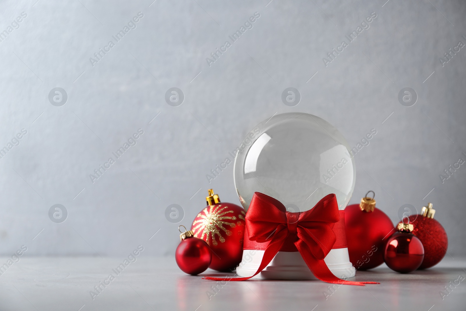 Photo of Beautiful Christmas snow globe with red bow and Christmas balls on grey table, space for text