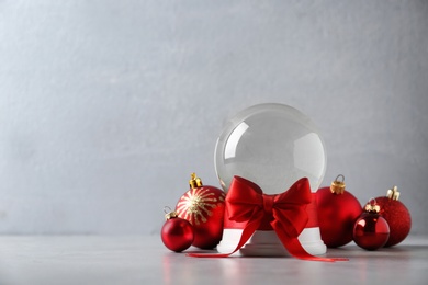 Photo of Beautiful Christmas snow globe with red bow and Christmas balls on grey table, space for text