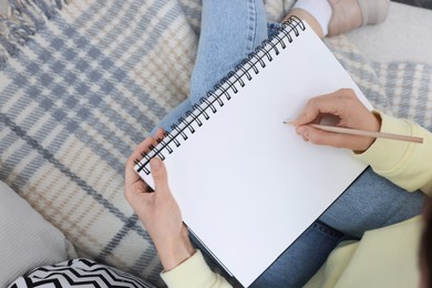 Photo of Young woman drawing in sketchbook on sofa, top view