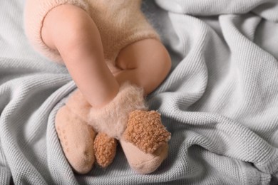 Photo of Cute newborn baby in knitted booties lying on light grey plaid, closeup of legs. Space for text