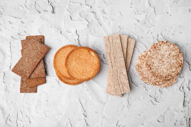 Photo of Rye crispbreads, rice cakes and rusks on white textured table, flat lay