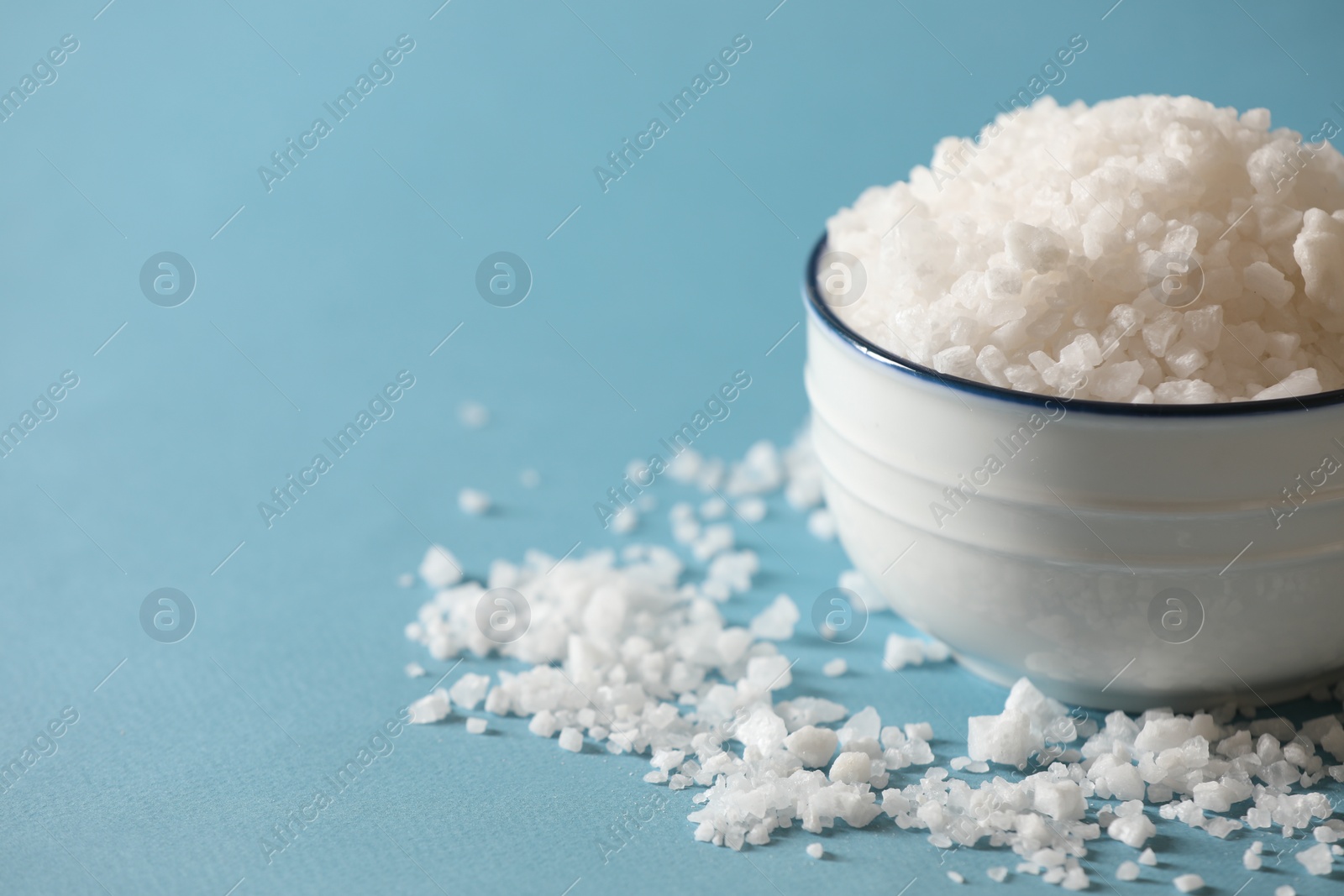 Photo of Organic salt in bowl on light blue background, closeup. Space for text