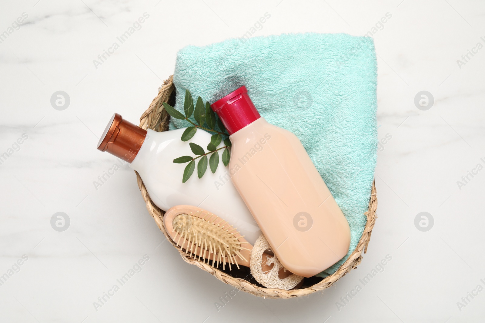 Photo of Shampoo bottles, hair brush, towel, loofah and leaves on white marble table, top view