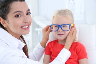 Photo of Children's doctor putting glasses on little girl in clinic