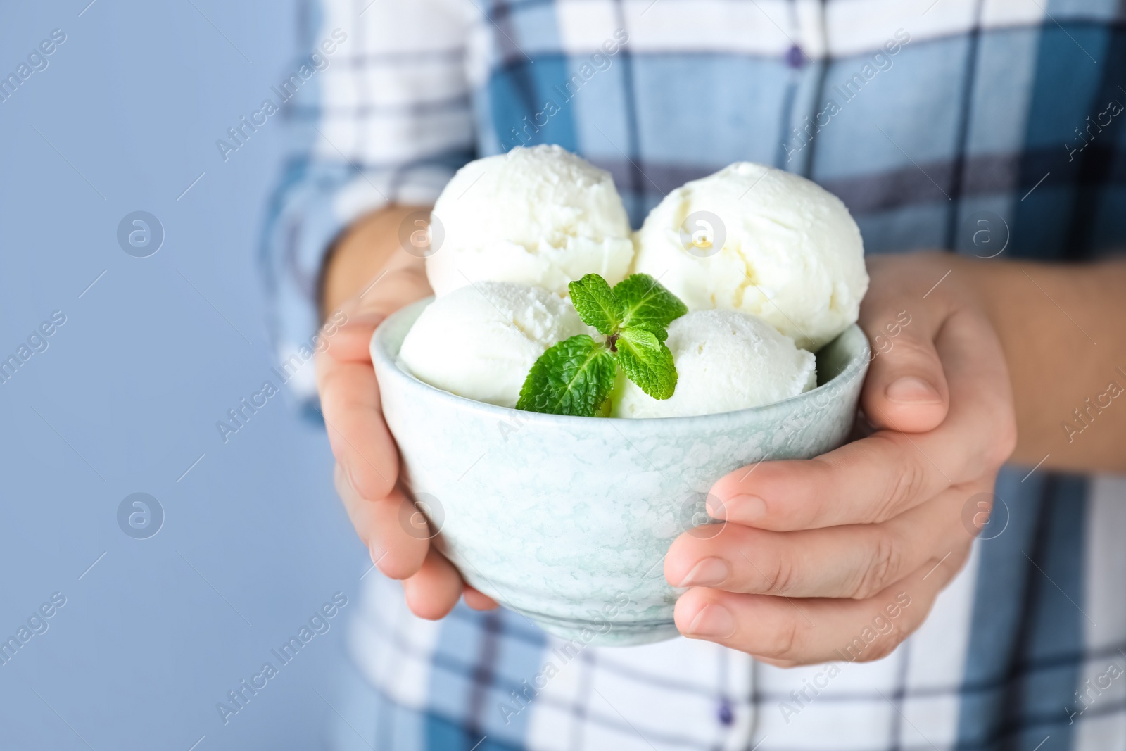 Photo of Woman holding bowl full of ice cream with mint on light grey background, closeup. Space for text