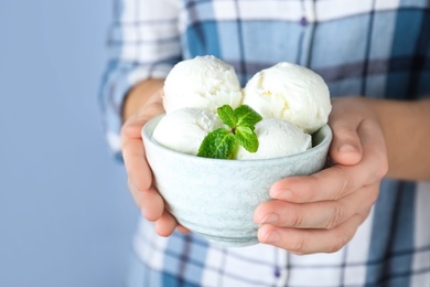 Photo of Woman holding bowl full of ice cream with mint on light grey background, closeup. Space for text