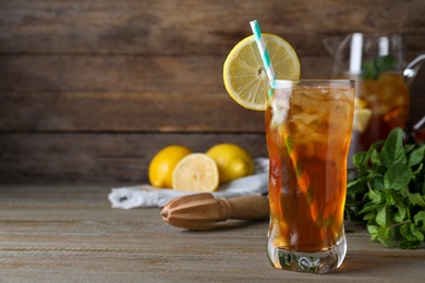 Delicious iced tea in glass on wooden table, space for text