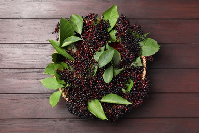 Photo of Ripe elderberries with green leaves on wooden table, top view