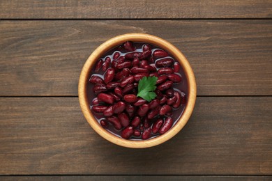 Photo of Bowl of canned red kidney beans with parsley on wooden table, top view