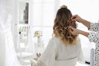 Photo of Professional stylist making wedding hairstyle for bride in salon, back view