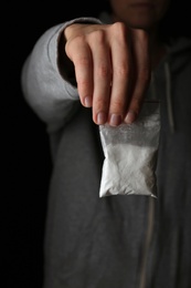 Photo of Drug dealer holding bag with cocaine on black background, closeup