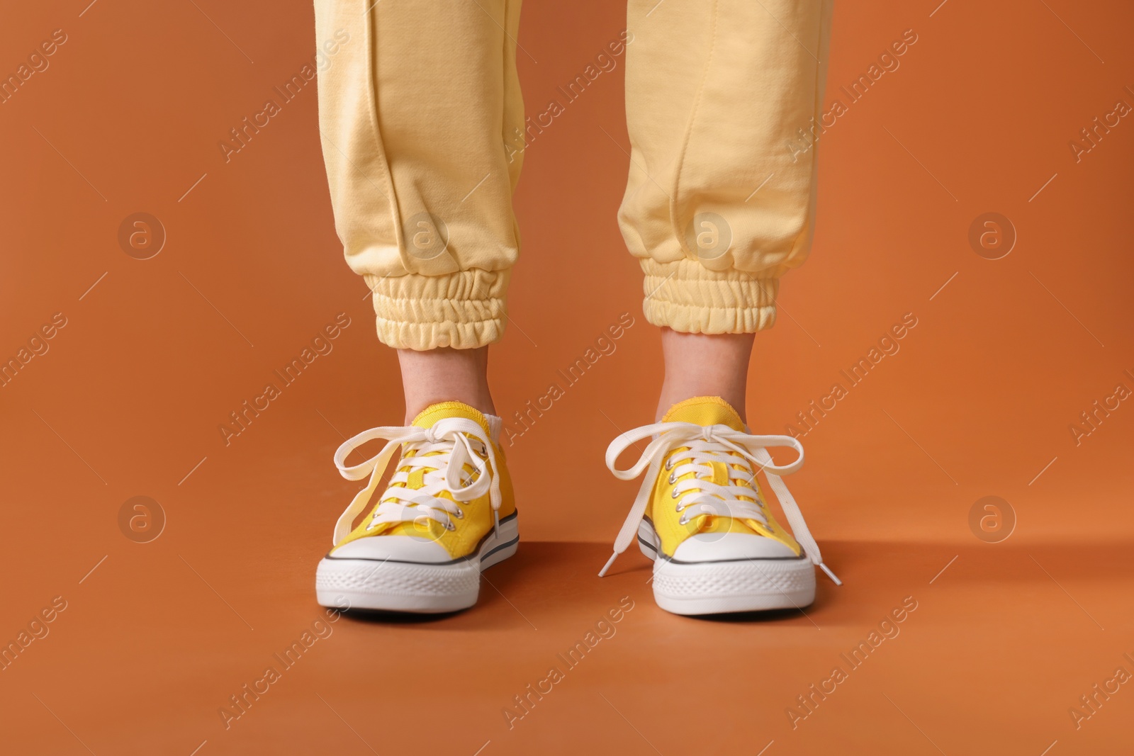 Photo of Woman wearing yellow classic old school sneakers on brown background, closeup