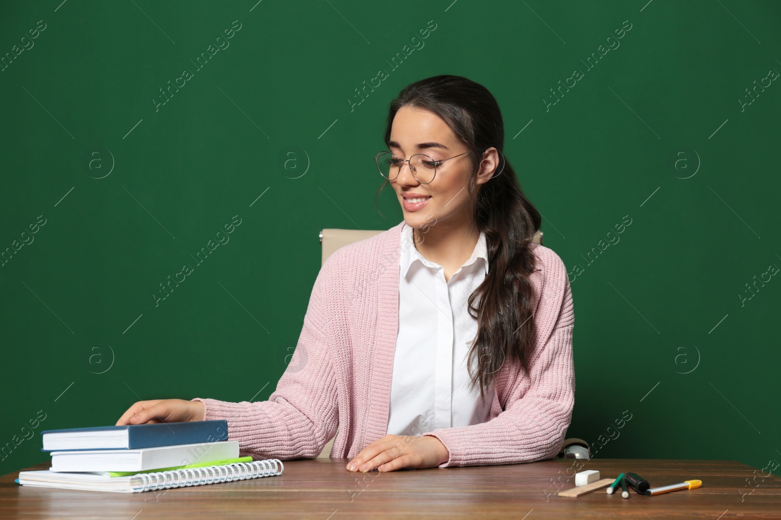 Photo of Portrait of beautiful young teacher sitting at table near chalkboard