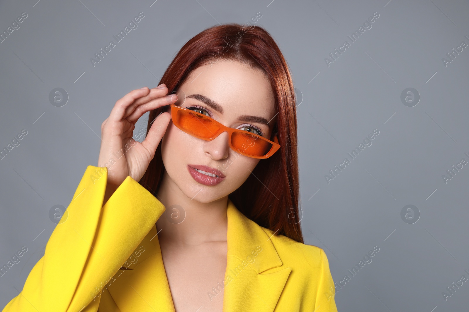 Photo of Stylish woman with red dyed hair and orange sunglasses on light gray background